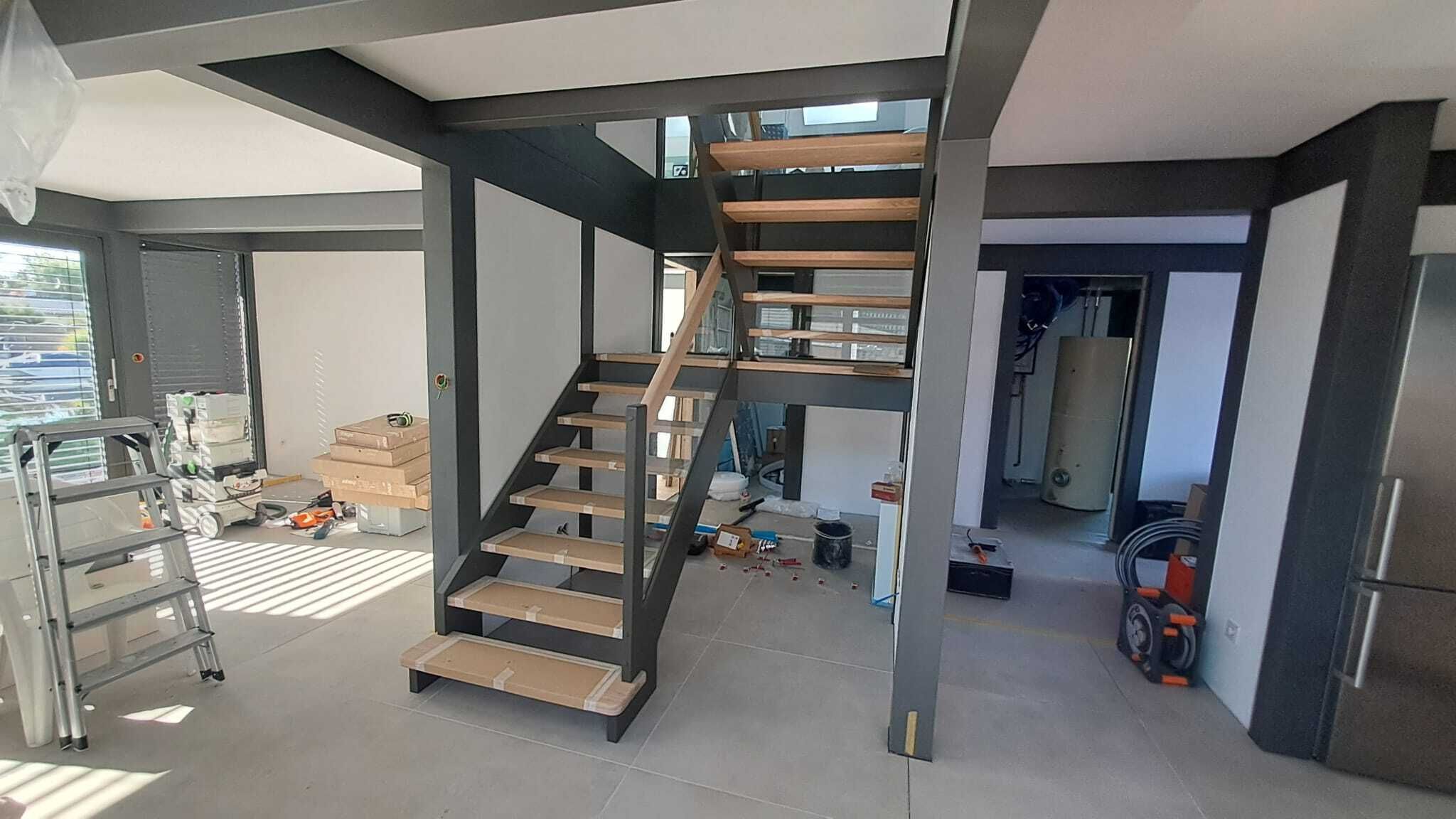 Treppe mit Podest, dunklen Stahlwangen und hellen Holzstufen mit Kantenschutz in einem Neubau vor der Fertigstellung