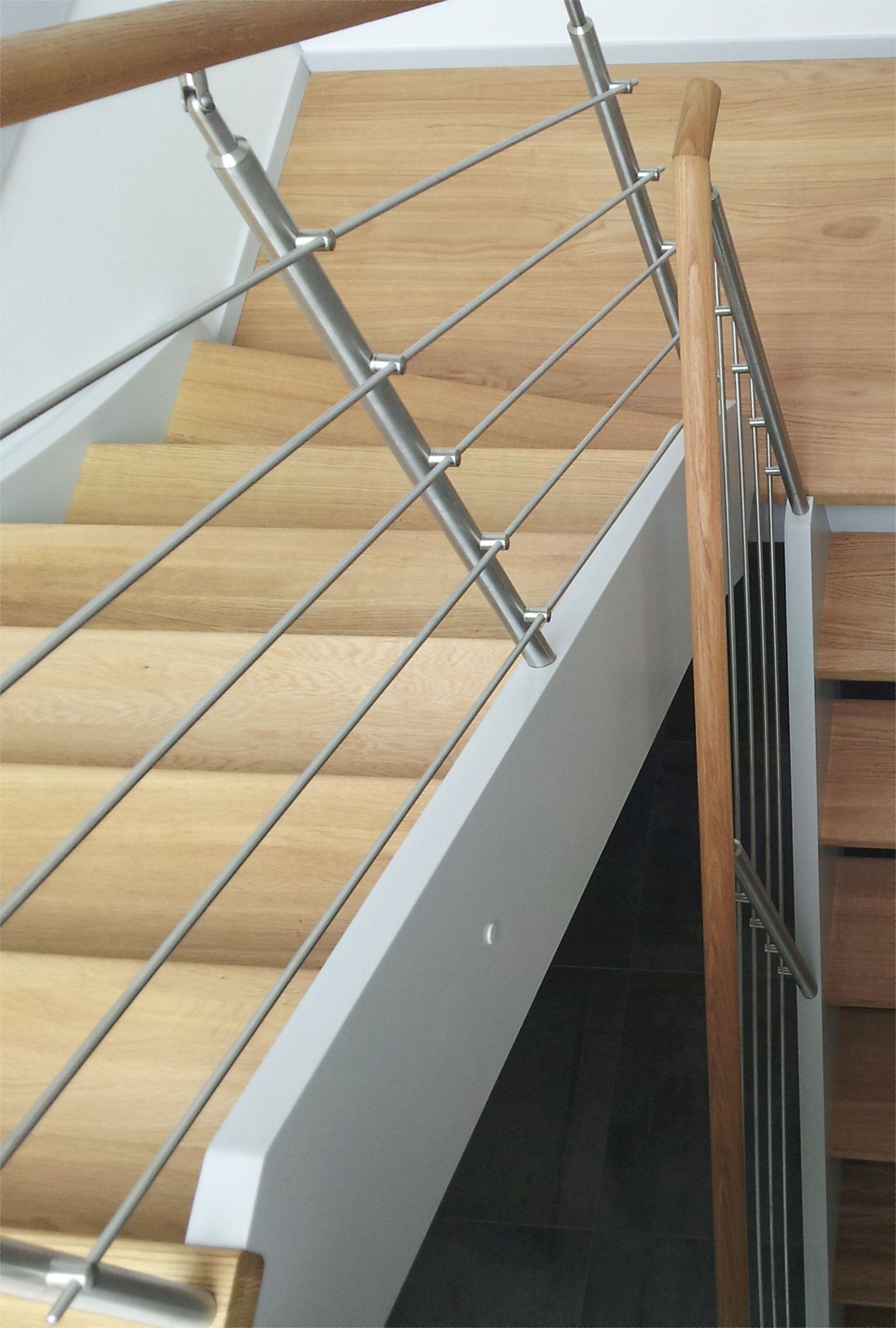 Gewendelte Treppe mit hellen Holzstufen, weißer Wange und Edelstahl-Relinggeländer mit Holzhandlauf, Blick von oben