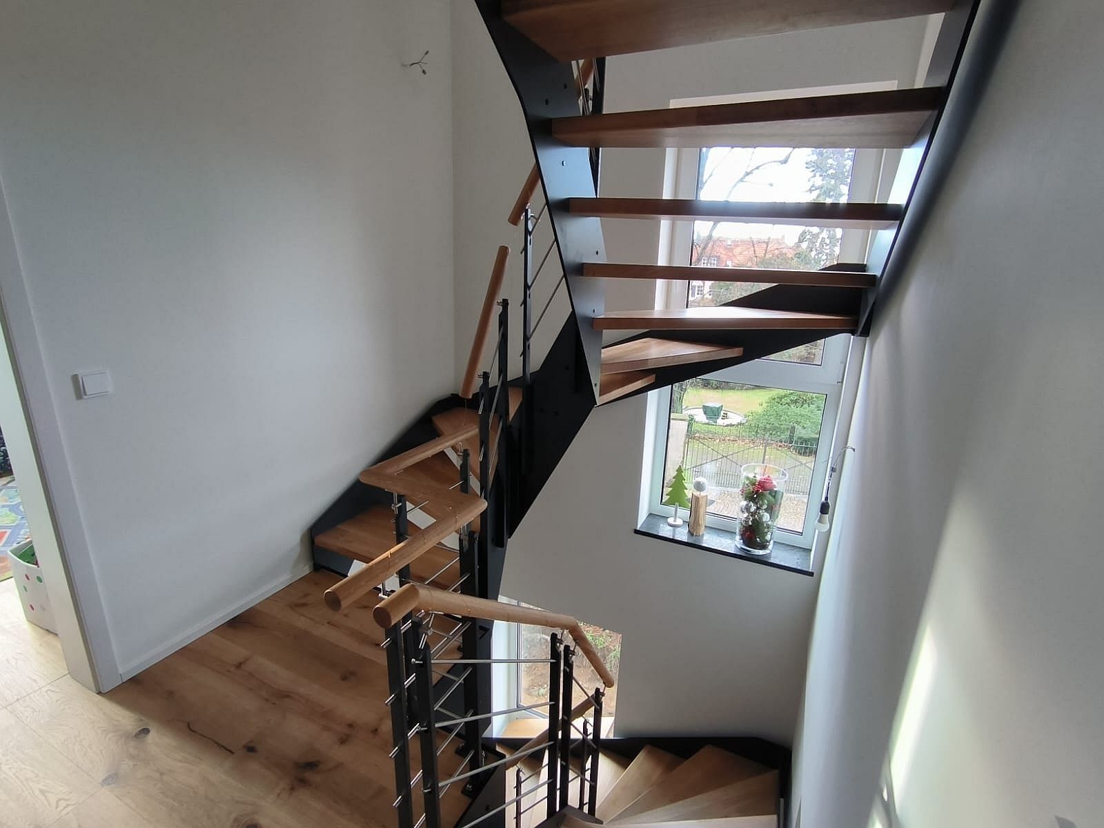 Gewendelte Treppe mit schwarzer Stahlwange und offenen Holzstufen im Treppenhaus mit Fenster, Blick von oben