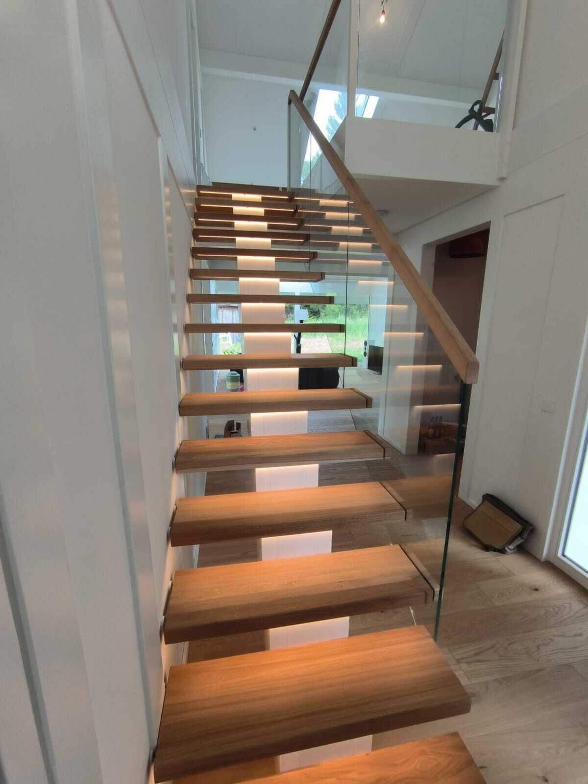 Gerade Treppe mit massiven Holzstufen, einseitig an der Wand befestigt, mit Glasgeländer und indirekter Beleuchtung