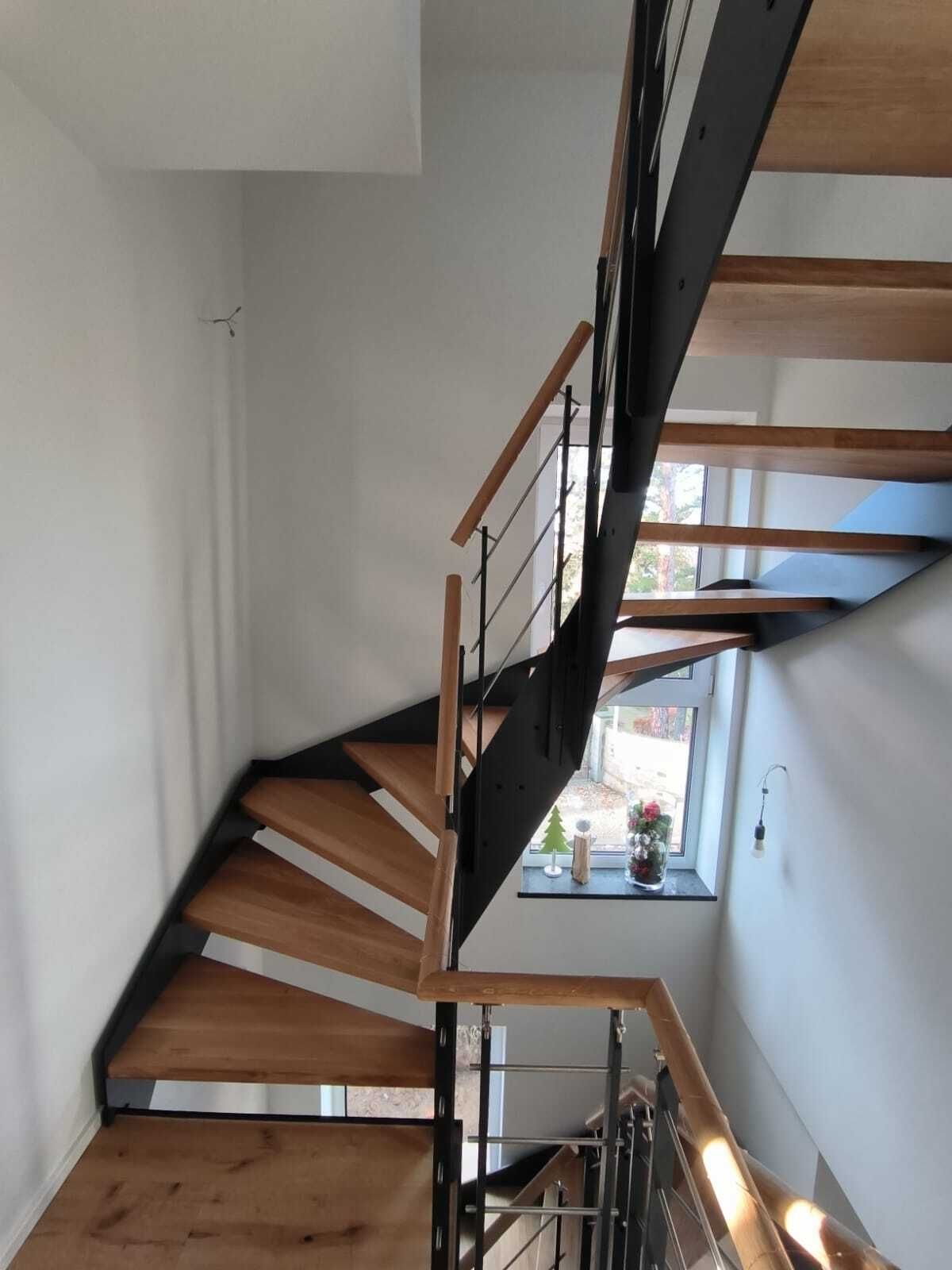 Gewendelte Treppe mit schwarzen Stahlwangen, offenen hellen Holzstufen und Holzhandlauf im Treppenhaus, Blick nach oben