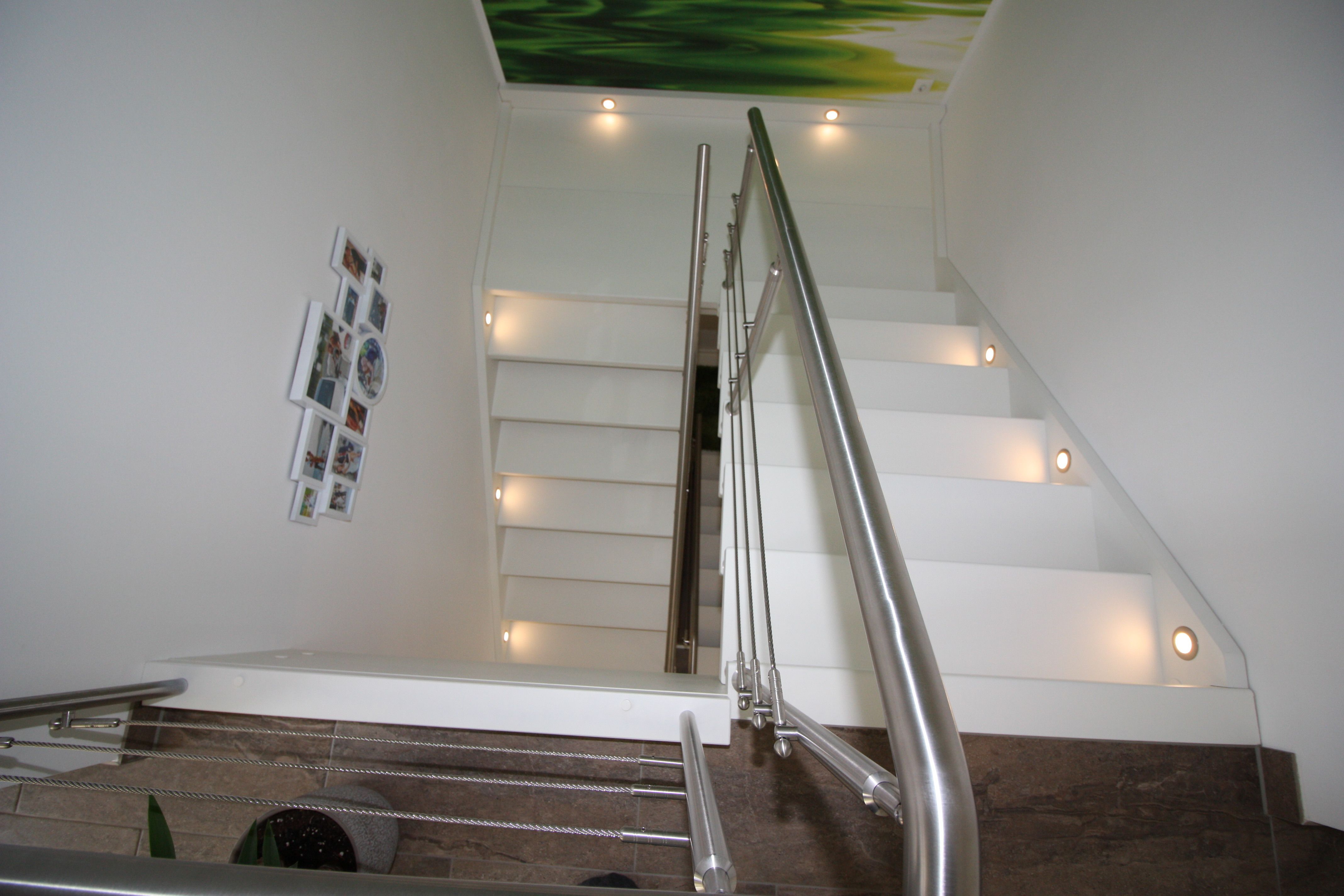 Weiße Treppe mit Podest, Stufenbeleuchtung in der Wand und Edelstahlhandlauf, Blick das Treppenhaus hinauf