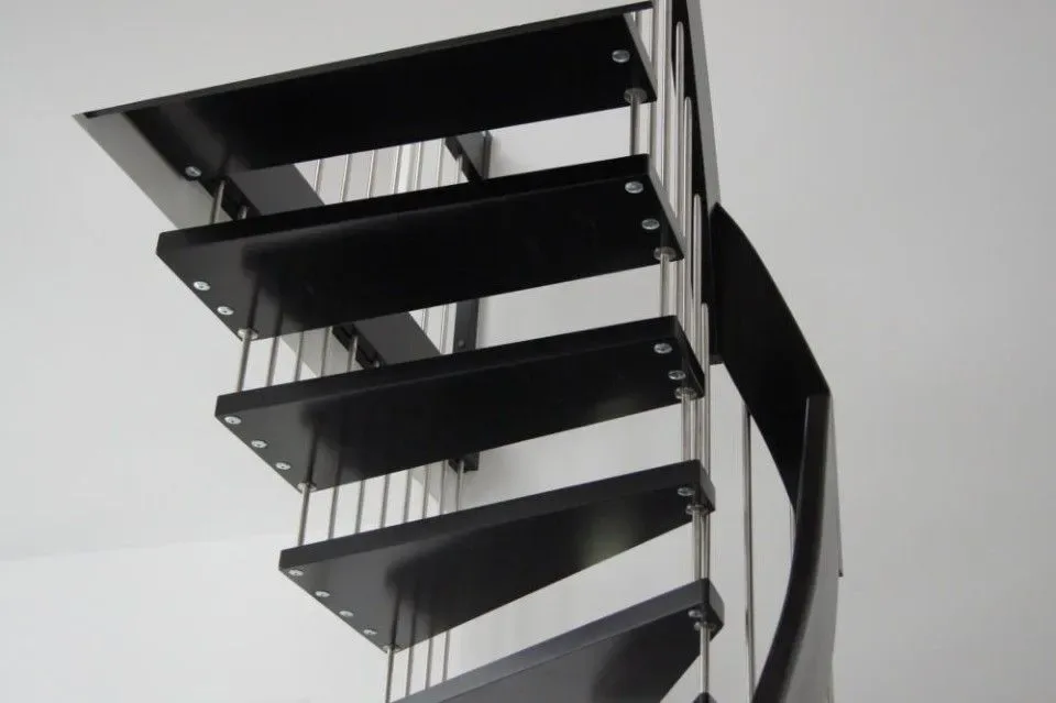Untersicht einer gewendelten Treppe mit schwarzen Stufen, verbunden durch Edelstahlstäbe, vor weißer Wand