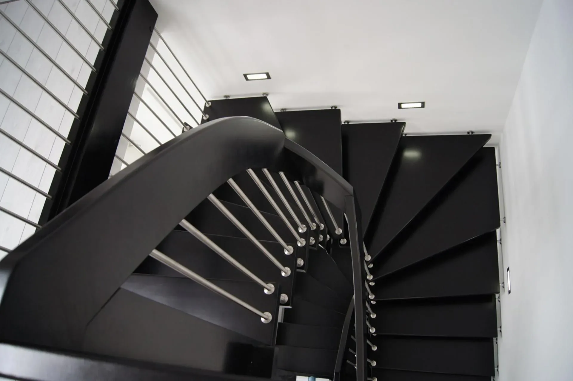 Gewendelte Treppe mit schwarzen Stufen, schwarzem Handlauf und Edelstahlstäben im Treppenhaus, Blick von oben