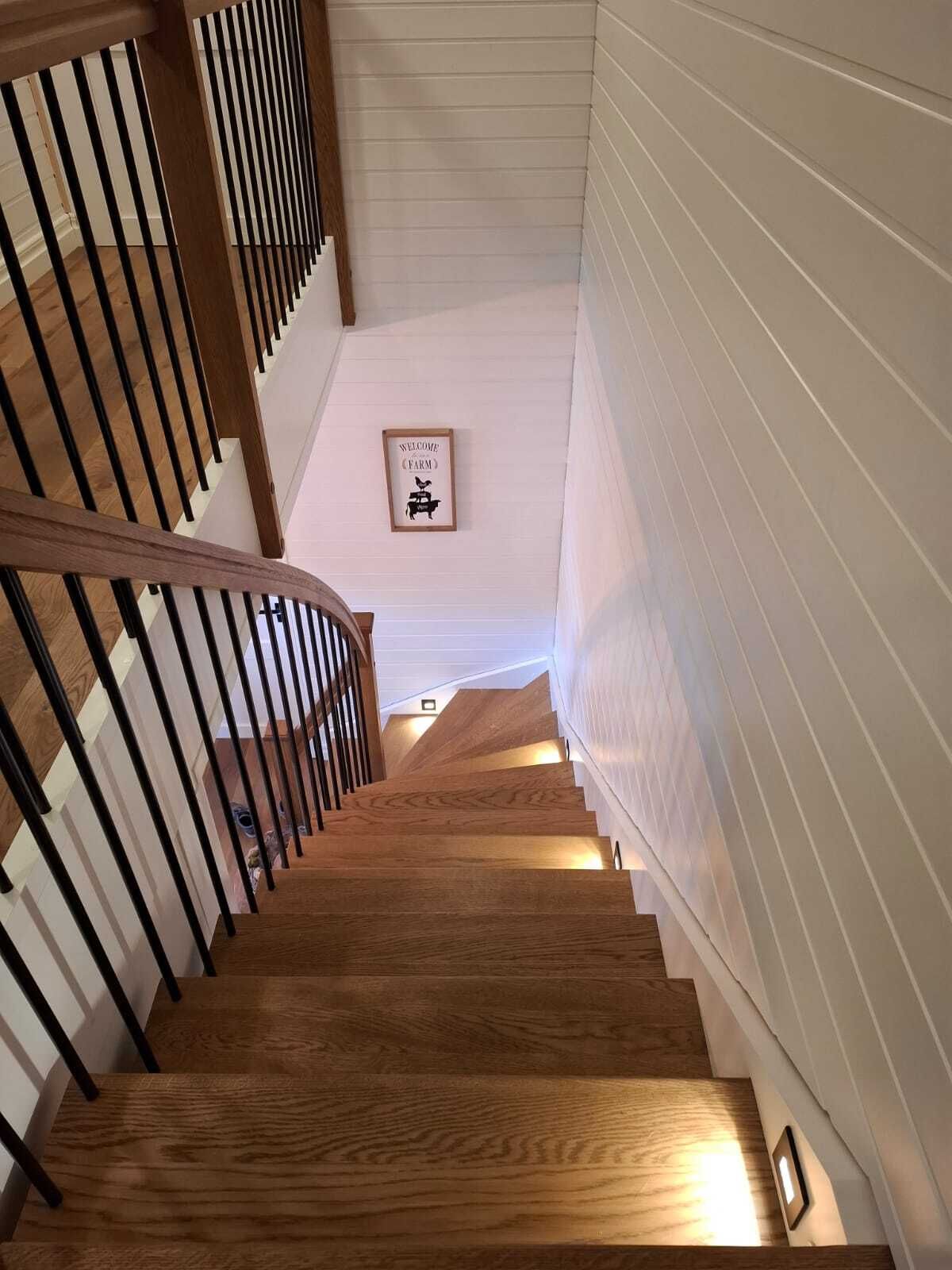 Blick von oben auf eine gewendelte Treppe mit Holzstufen, schwarzen Metallstäben und Holzhandlauf