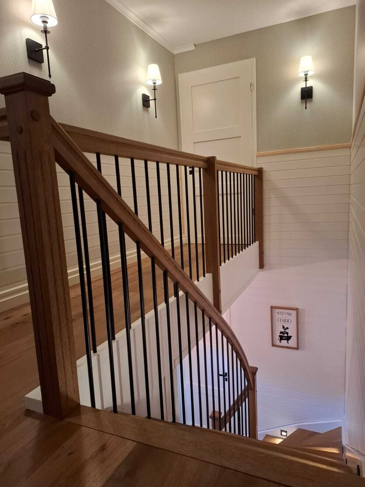 Treppengeländer mit Holzpfosten, Holzhandlauf und schwarzen Metallstäben an der Galerie, Blick hinab ins Treppenhaus