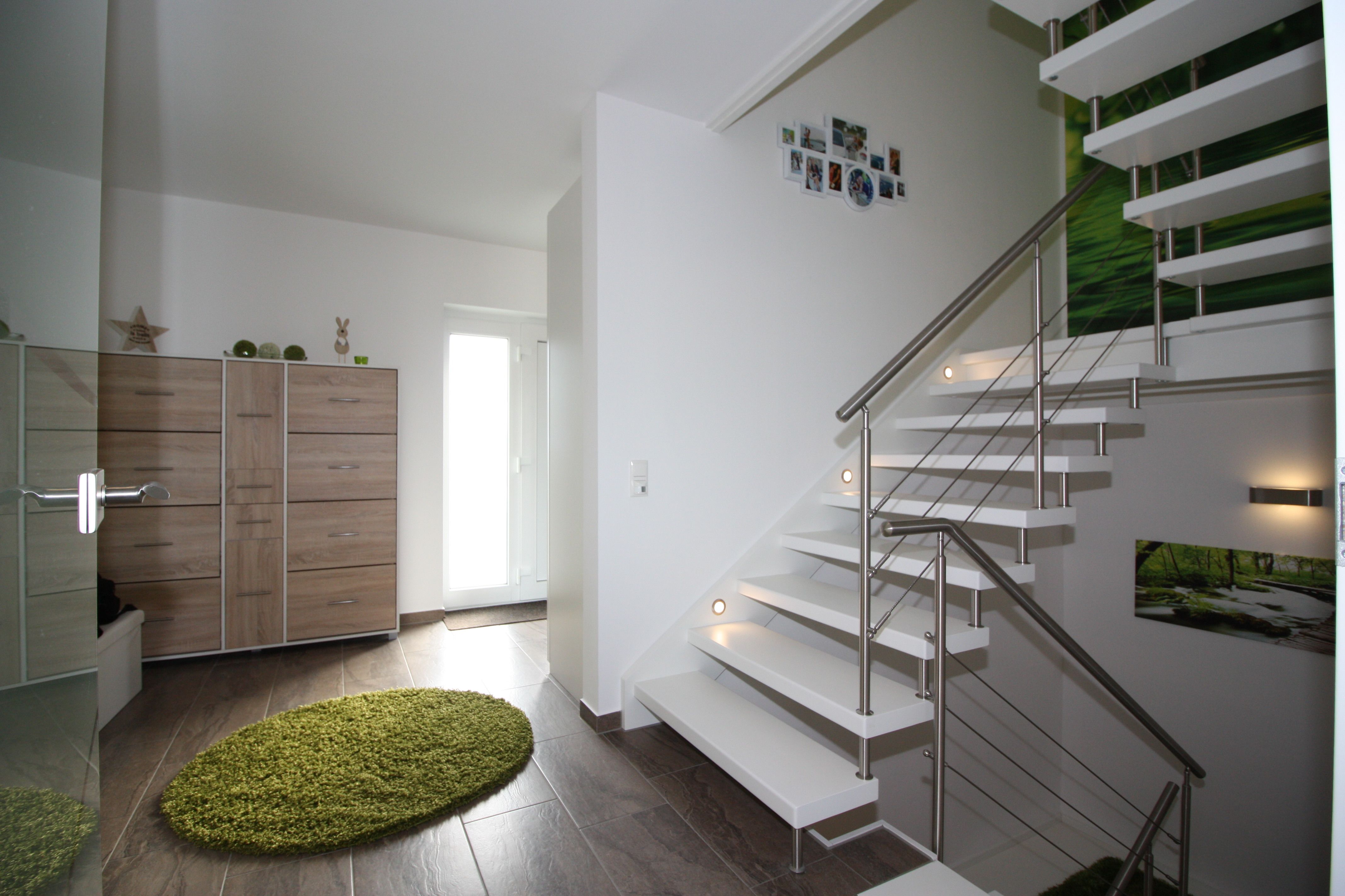 Weiße gewendelte Treppe mit Edelstahlgeländer und Stufenbeleuchtung in der Wand, in einer hellen Diele