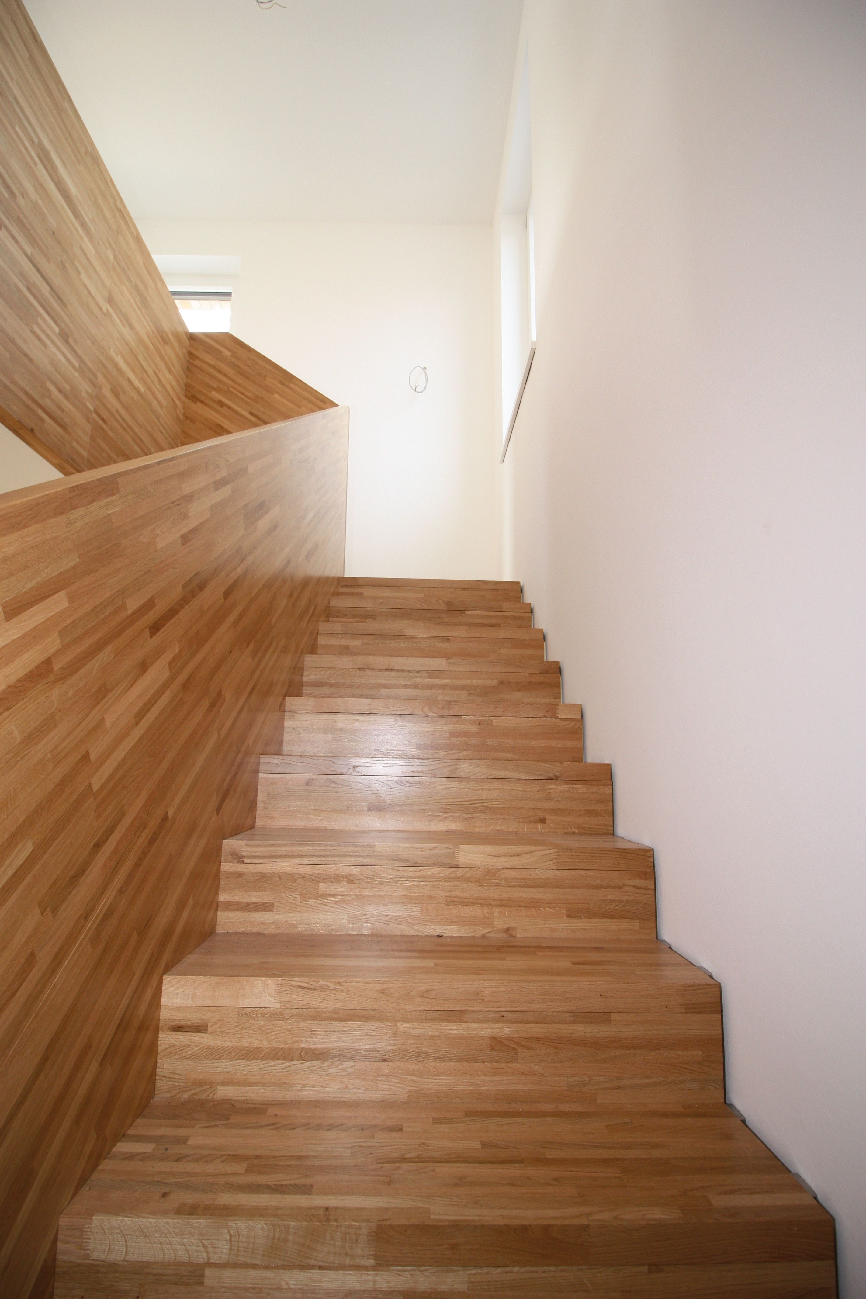 Gerade Treppe mit Stufen und geschlossener Brüstung aus hellem, stabverleimtem Holz, Blick hinauf zum Podest