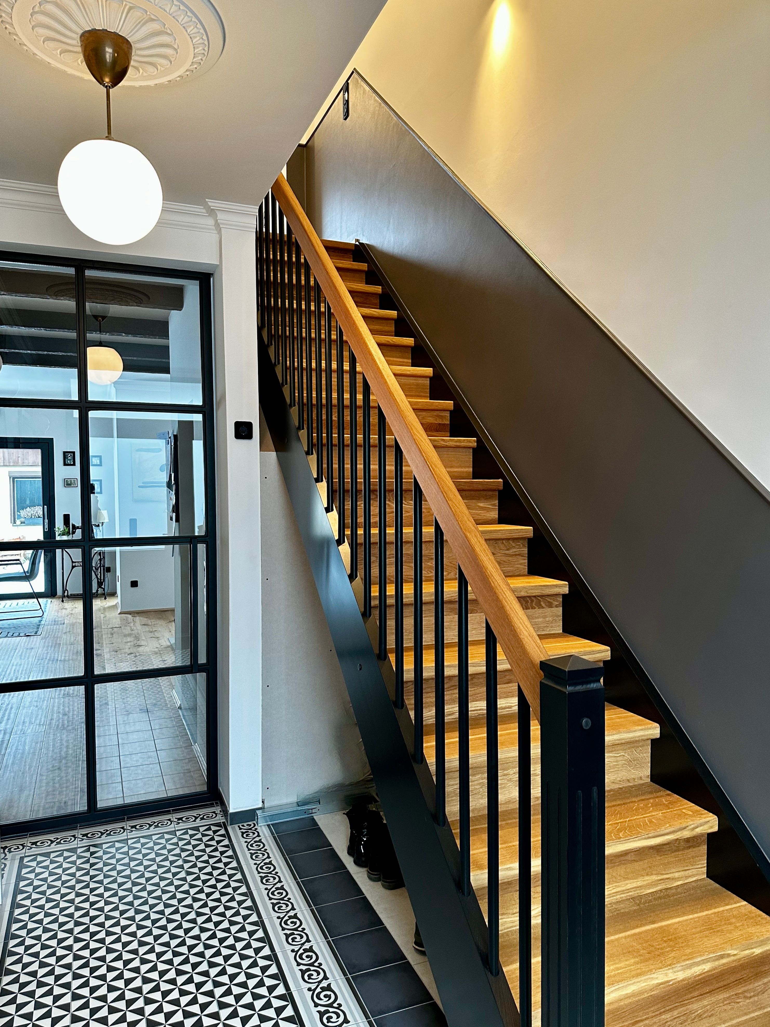 Gerade Treppe mit hellen Holzstufen, dunkler Wange und schwarzem Stabgeländer mit Holzhandlauf in einem Flur