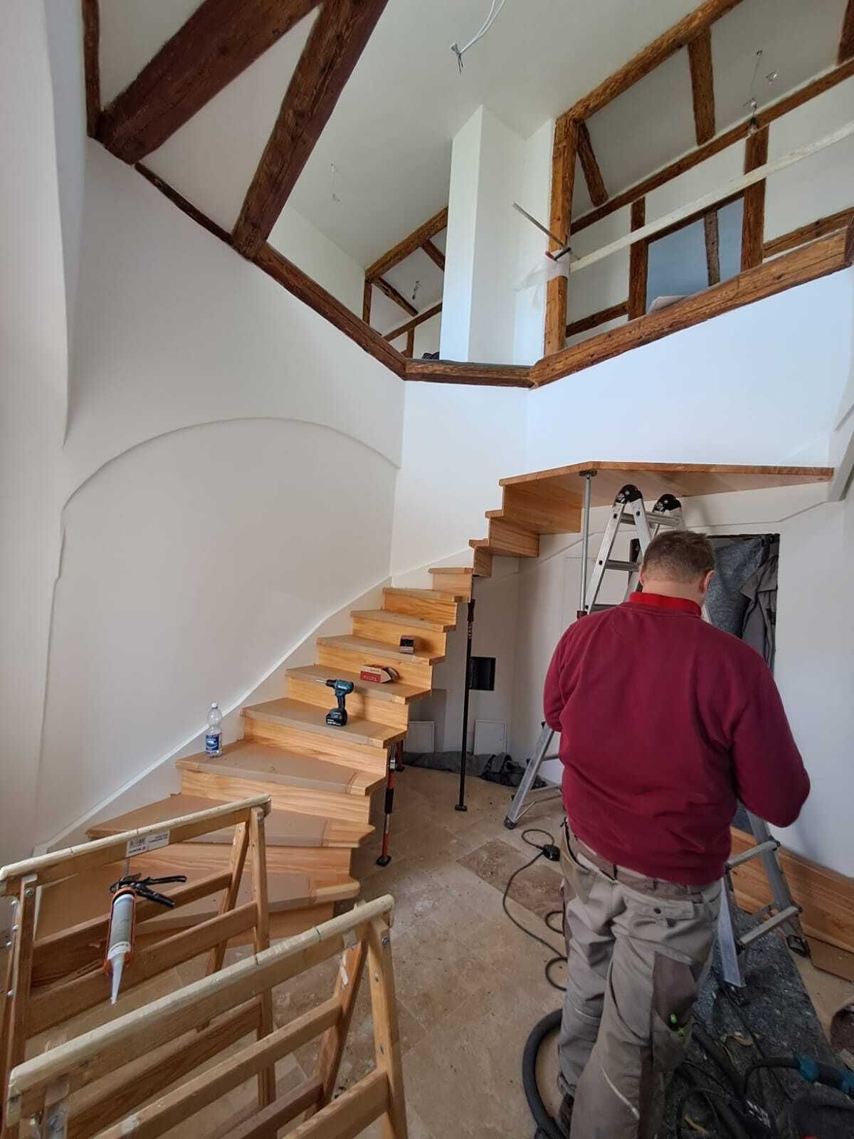 Monteur beim Einbau einer gewendelten Treppe mit hellen Holzstufen in einem Altbau mit Fachwerkgalerie