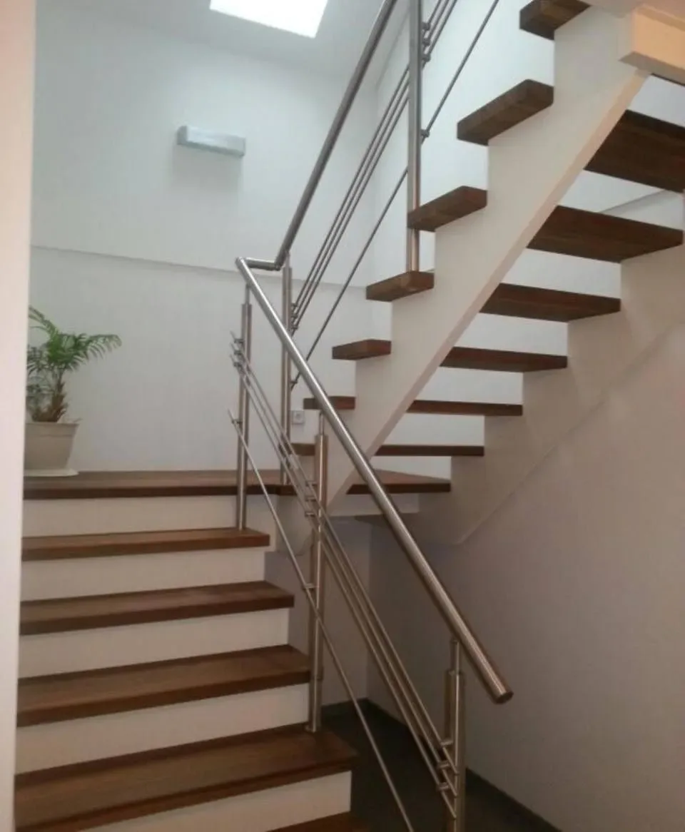 Podesttreppe mit dunklen Holzstufen, weißen Setzstufen und Edelstahlgeländer im Treppenhaus mit Oberlicht