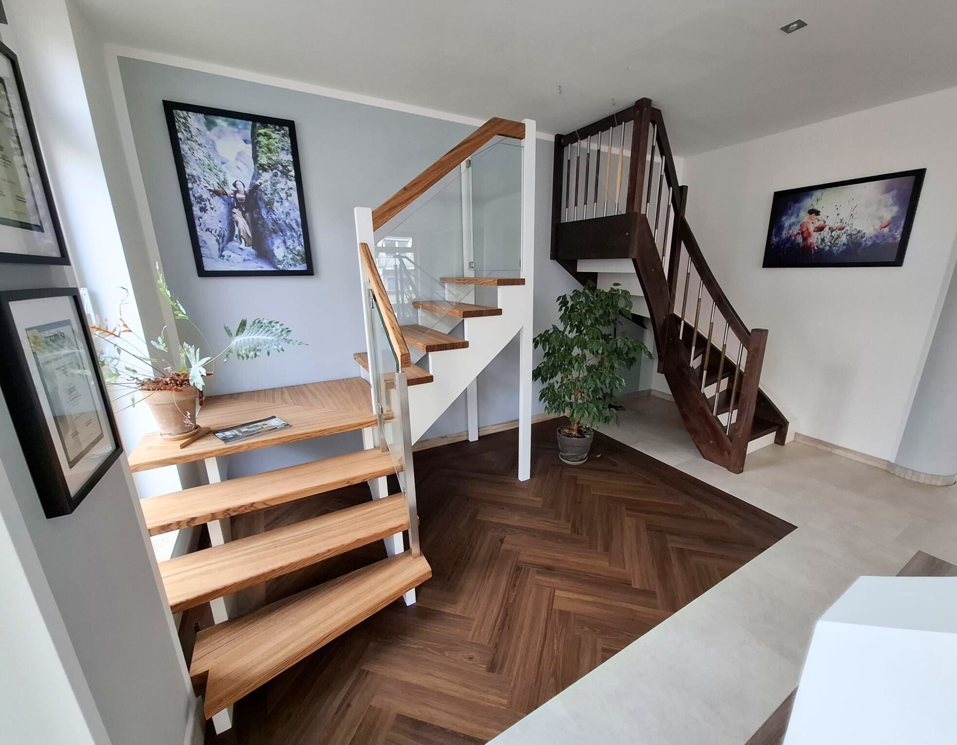 Zwei Treppen in der Ausstellung Dresden – halbgewendelte Treppe mit Eichenstufen und Glasgeländer, dahinter eine dunkle Wangentreppe mit Edelstahlstäben
