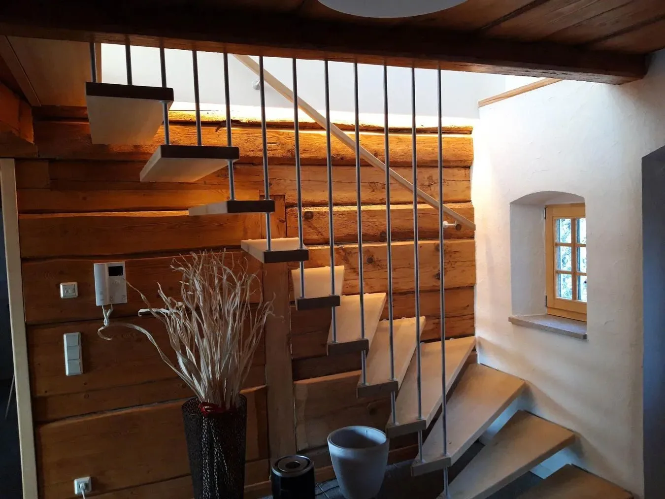 Gewendelte Treppe mit hellen, an Edelstahlstäben abgehängten Stufen vor einer Wand aus Holzbohlen