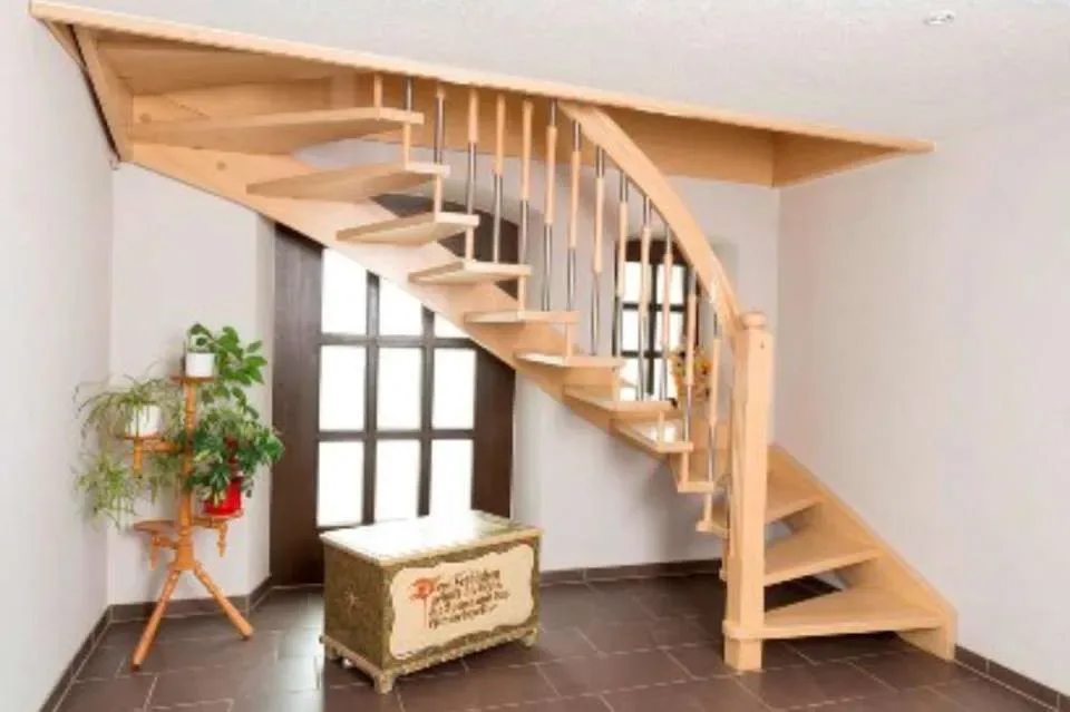 Gewendelte Wangentreppe aus hellem Holz mit offenen Stufen und Geländer aus Holz und Edelstahl in einer Diele